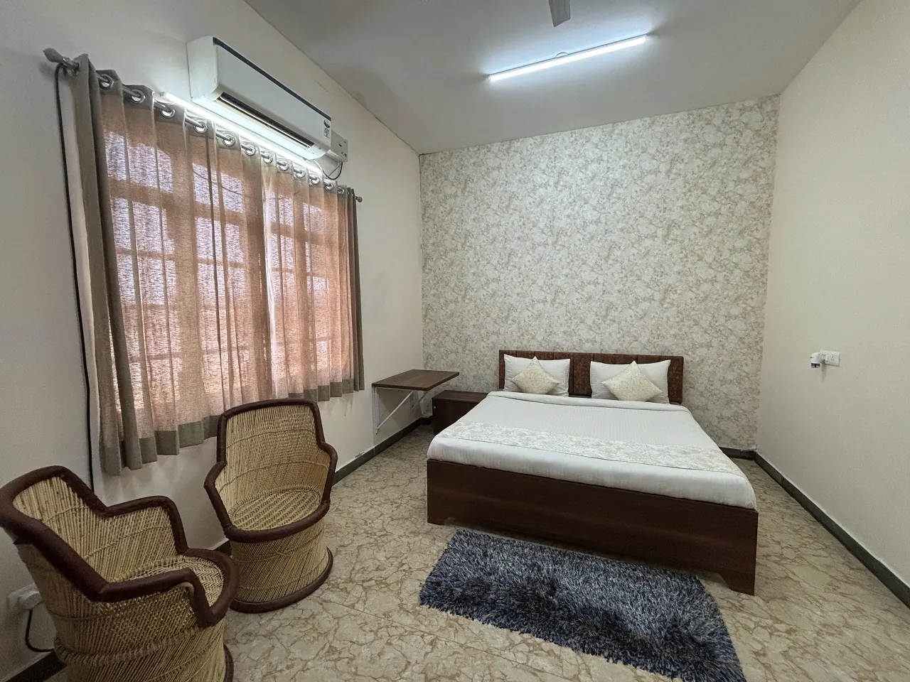 Spacious AC room with a double bed and cane chairs at Guru Kripa Hotel, Agolai